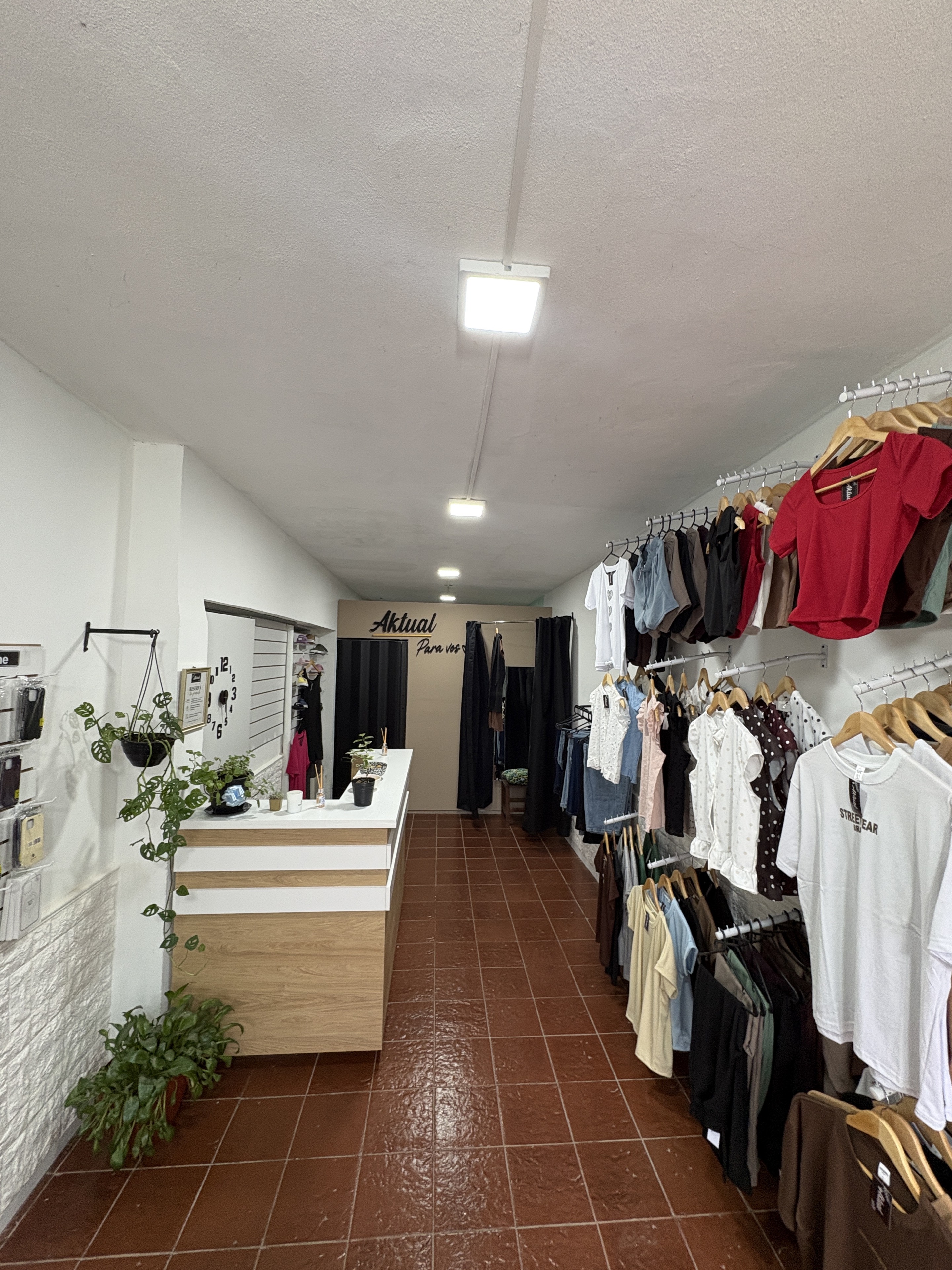 Interior de Aktual, con prendas en percheros, mostrador y plantas